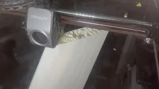 Enclosed 3D printer printing a tall white wing section; a close-up through the glass shows the printhead over the part's internal pattern