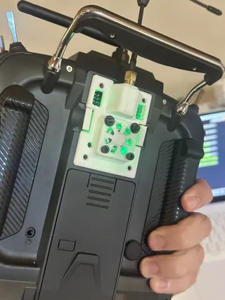 Back of a handheld RC transmitter fitted with a white 3D-printed module adapter and external antenna connector, glowing green