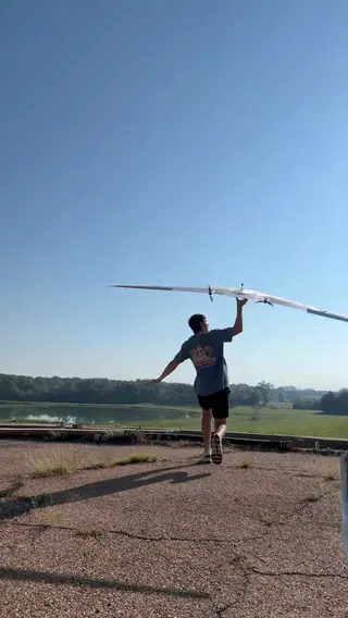A person runs across cracked pavement and hand-launches a large white flying wing with two spinning rear propellers