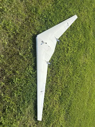 Top-down view of a white 3D-printed swept flying wing with twin pusher motors lying on bright green grass